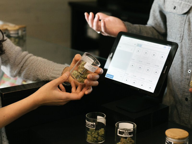 Hands holding a jar of cannabis in front of a cash register